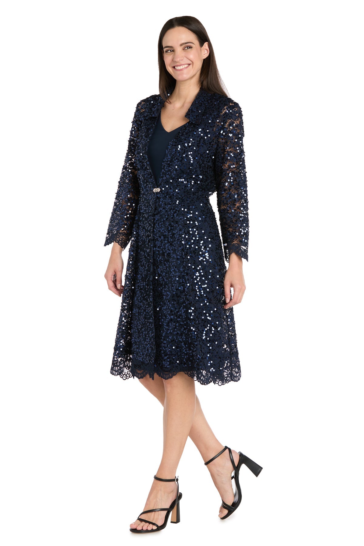 A woman wearing the R&M Richards 3742 Short Navy Jacket Party Dress, featuring sequined lace over a dark evening dress and paired with black high-heeled sandals.